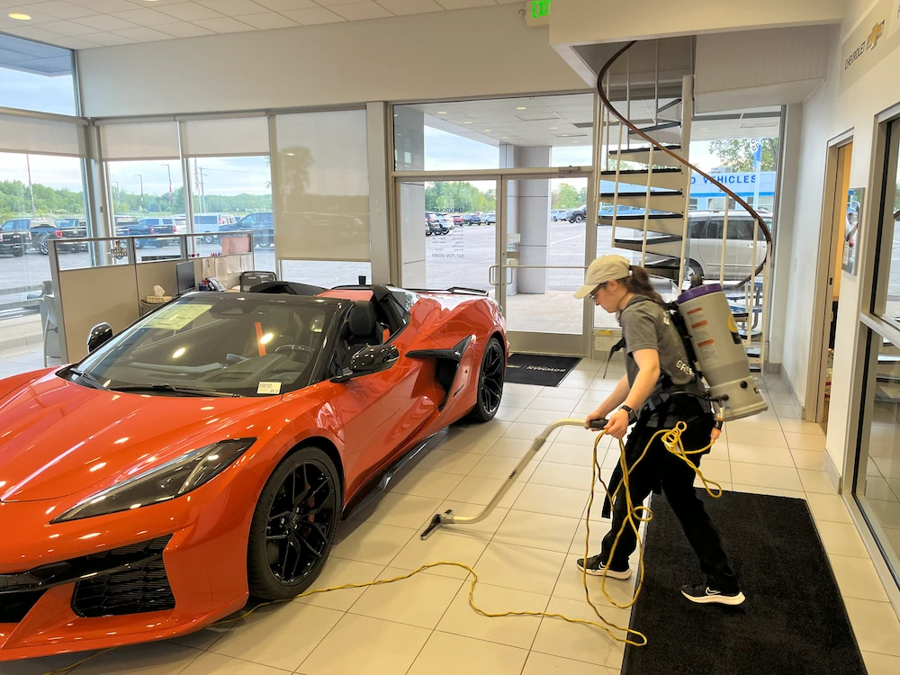 Cleaning person vacuuming new car showroom floor