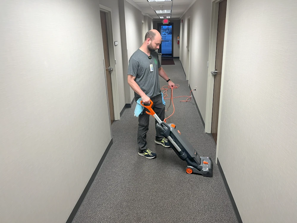 Janitorial service worker using vacuum to clean hallway of offices