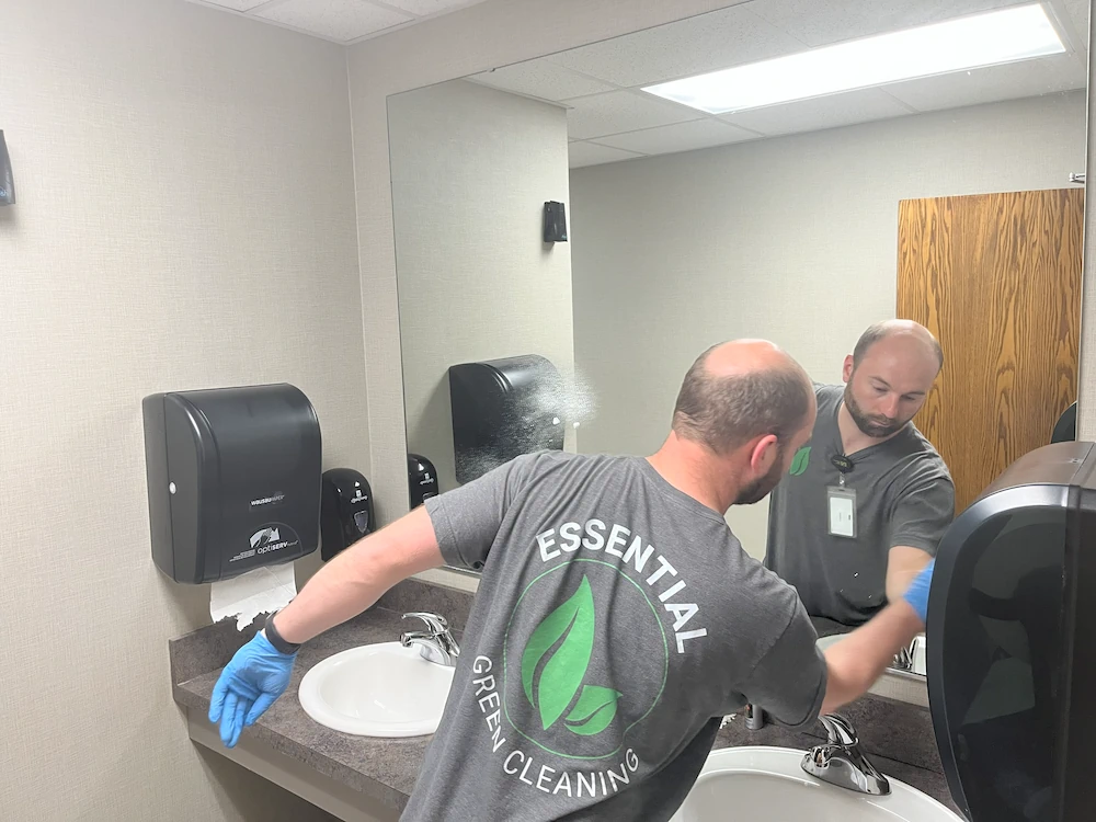 Janitorial cleaner wiping mirror in bathroom during regular office cleaning