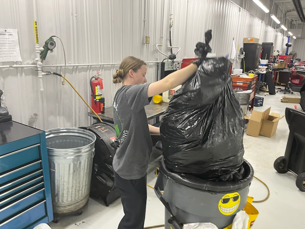 Janitorial worker removing trash from auto shop work area