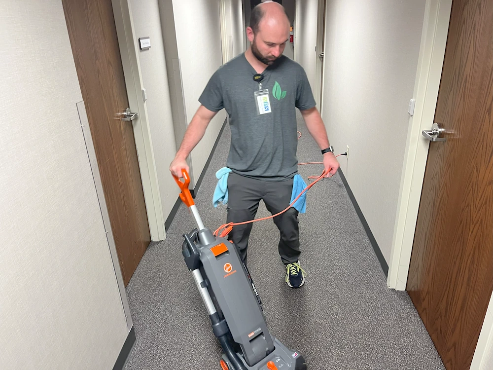 Janitorial cleaner vacuuming hallway at office building